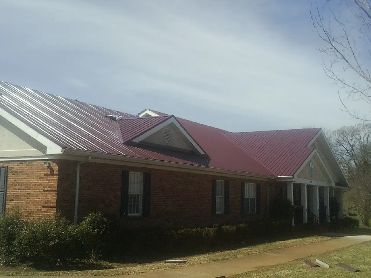 Red metal roof with gabled entries on a long brick building, from a Hail Damage Roof Repair job in Merrillville