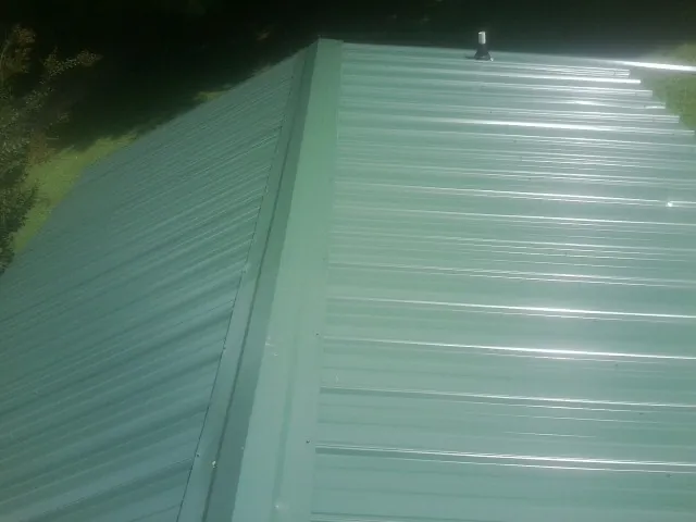New green metal panels meeting at the ridge of a roof — Flat Roof Repair work by our crew in Merrillville