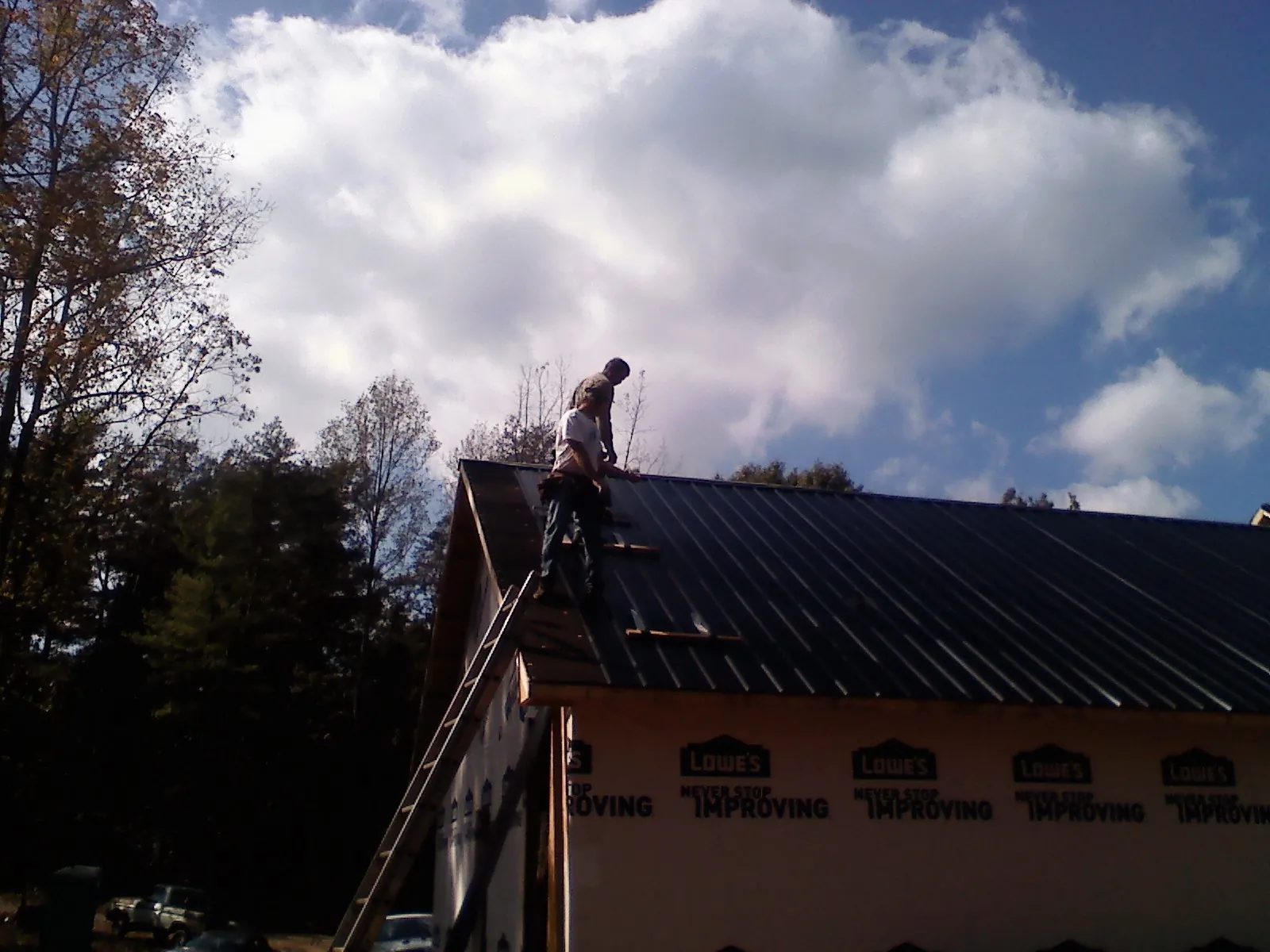 Roofer fastening dark metal panels high against a cloudy sky, from a Roof Inspection job in Merrillville