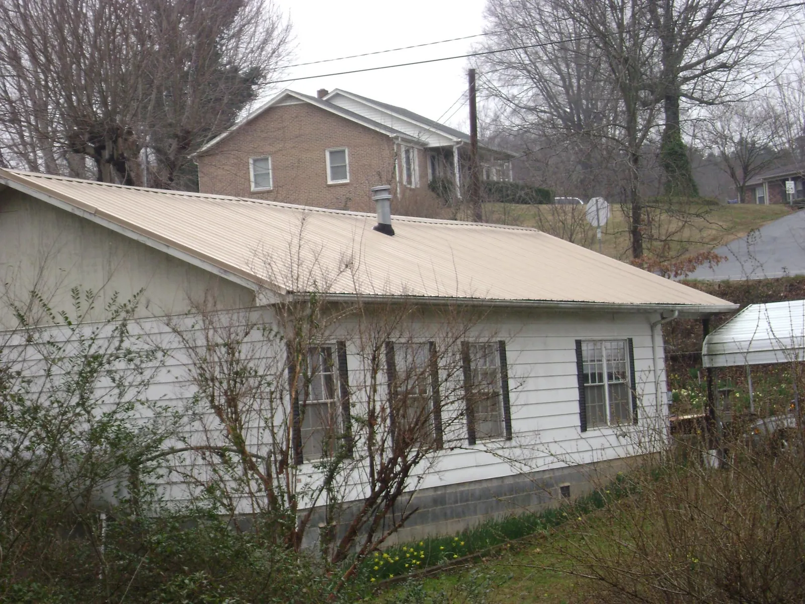 Tan metal roof on a white sided house set into a hillside — Commercial Roofing by Roofing Brothers in Merrillville